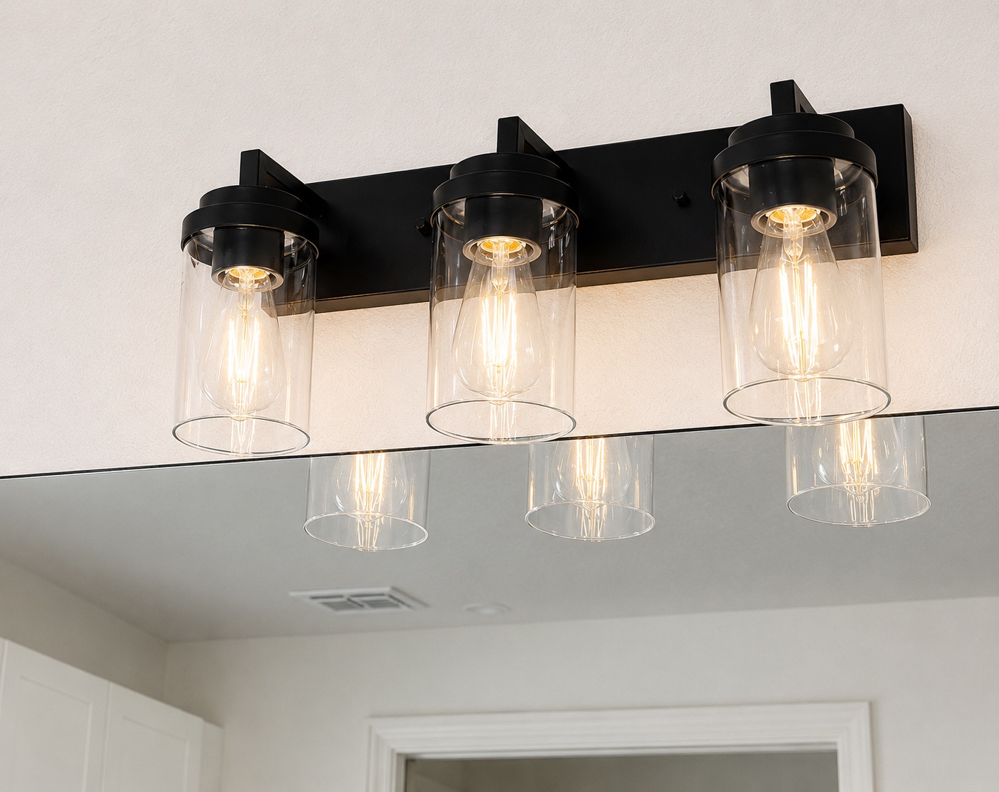 Black vanity light fixture with three Edison-bulb sconces installed over a bathroom mirror